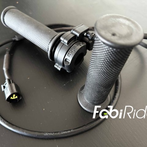 Juodos guminės elektrinio motociklo vairo rankenos (grips) su prijungimo laidu „FabiRide“ fone.